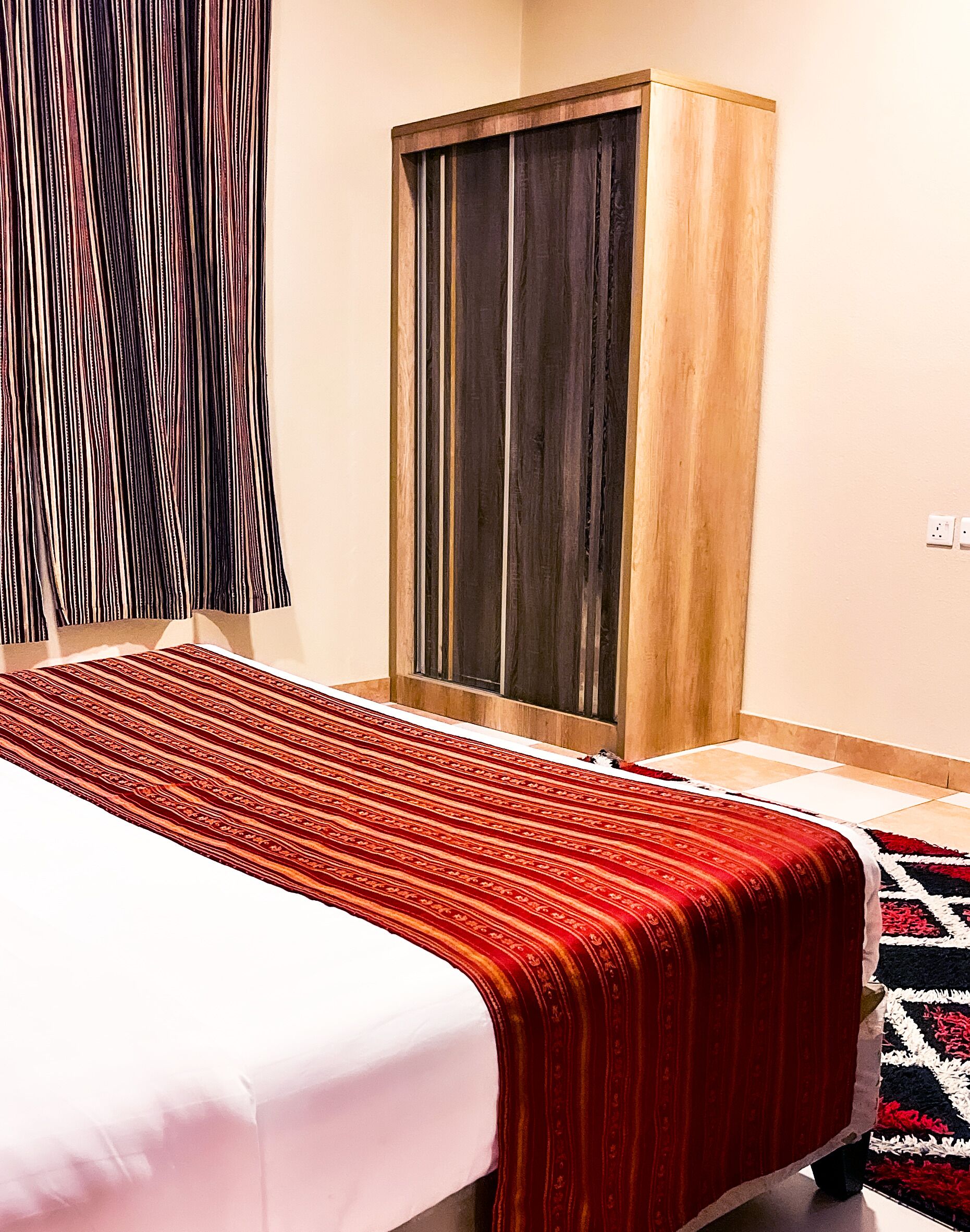 A hotel room with a bed, a wardrobe, a window, and a wall socket.