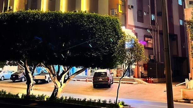 A multi-story hotel with illuminated signage, a central entrance, and a parking area with cars. - Alora Zone (Abha)