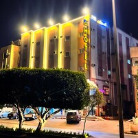A multi-story hotel with illuminated signage, a central entrance, and a parking area with cars.