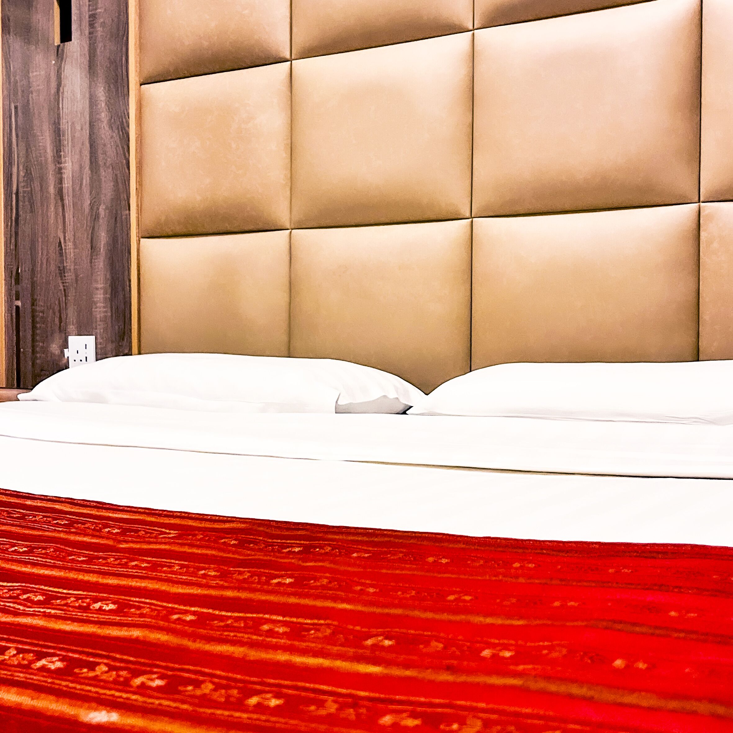 A bed with a tufted headboard, white bedding, and a red patterned carpet.