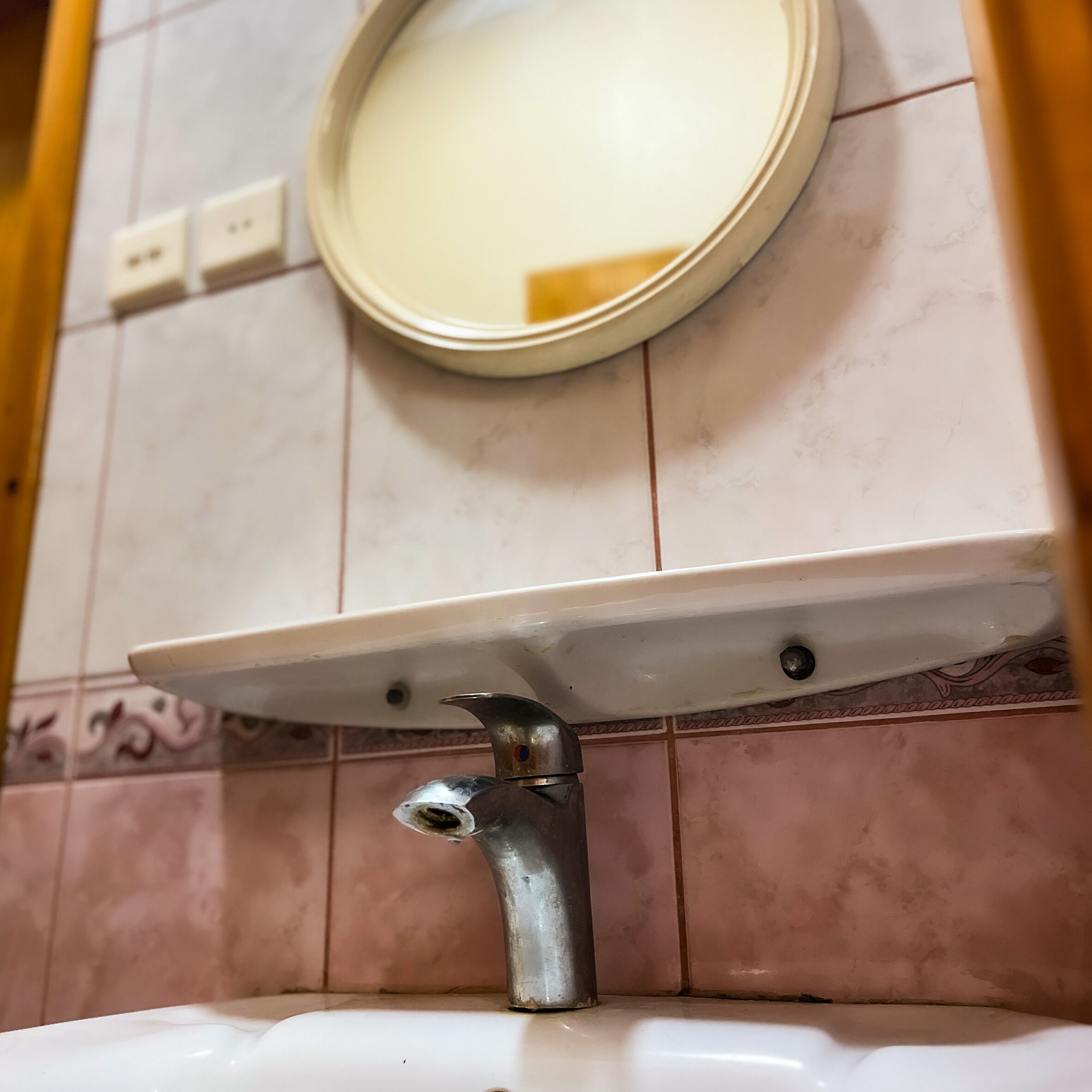 Un lavabo dans une salle de bain, avec un miroir au-dessus, fixé sur un mur recouvert de carreaux.