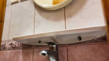 Un lavabo dans une salle de bain, avec un miroir au-dessus, fixé sur un mur recouvert de carreaux.