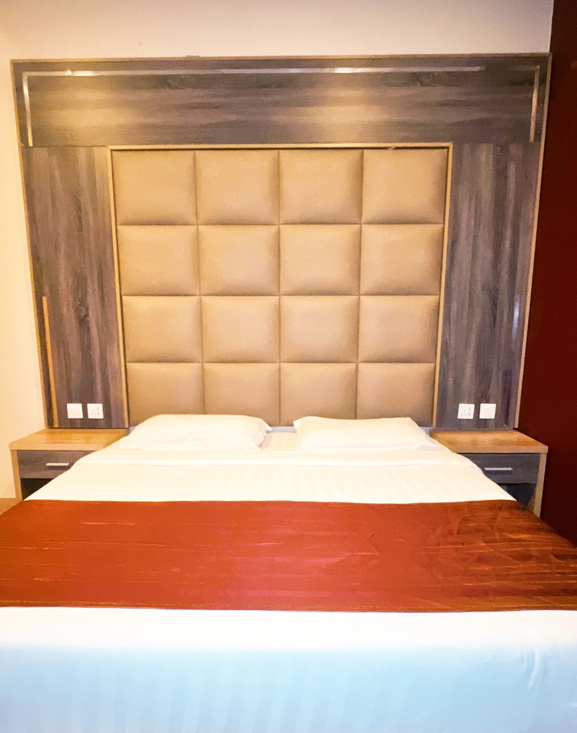A bed with a headboard, two bedside tables, and a red bedspread.