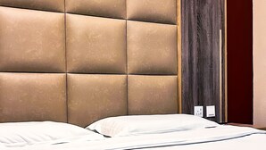 A hotel room with a tufted headboard, a bed with white linens, and a dark wooden door. - Alora Zone (Abha)