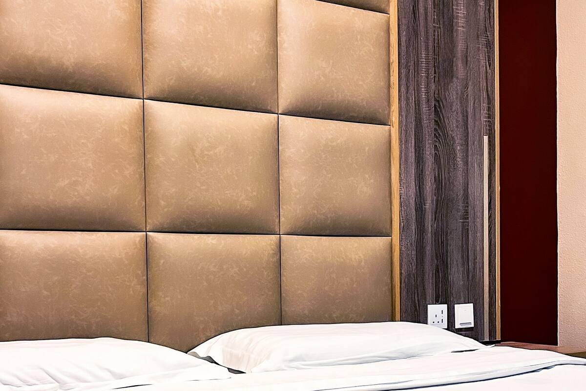 A hotel room with a tufted headboard, a bed with white linens, and a dark wooden door.