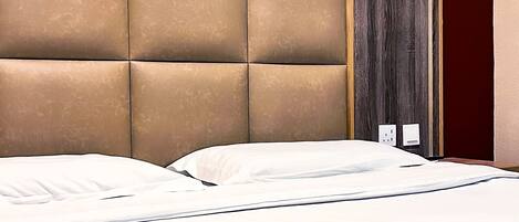 A hotel room with a tufted headboard, a bed with white linens, and a dark wooden door.