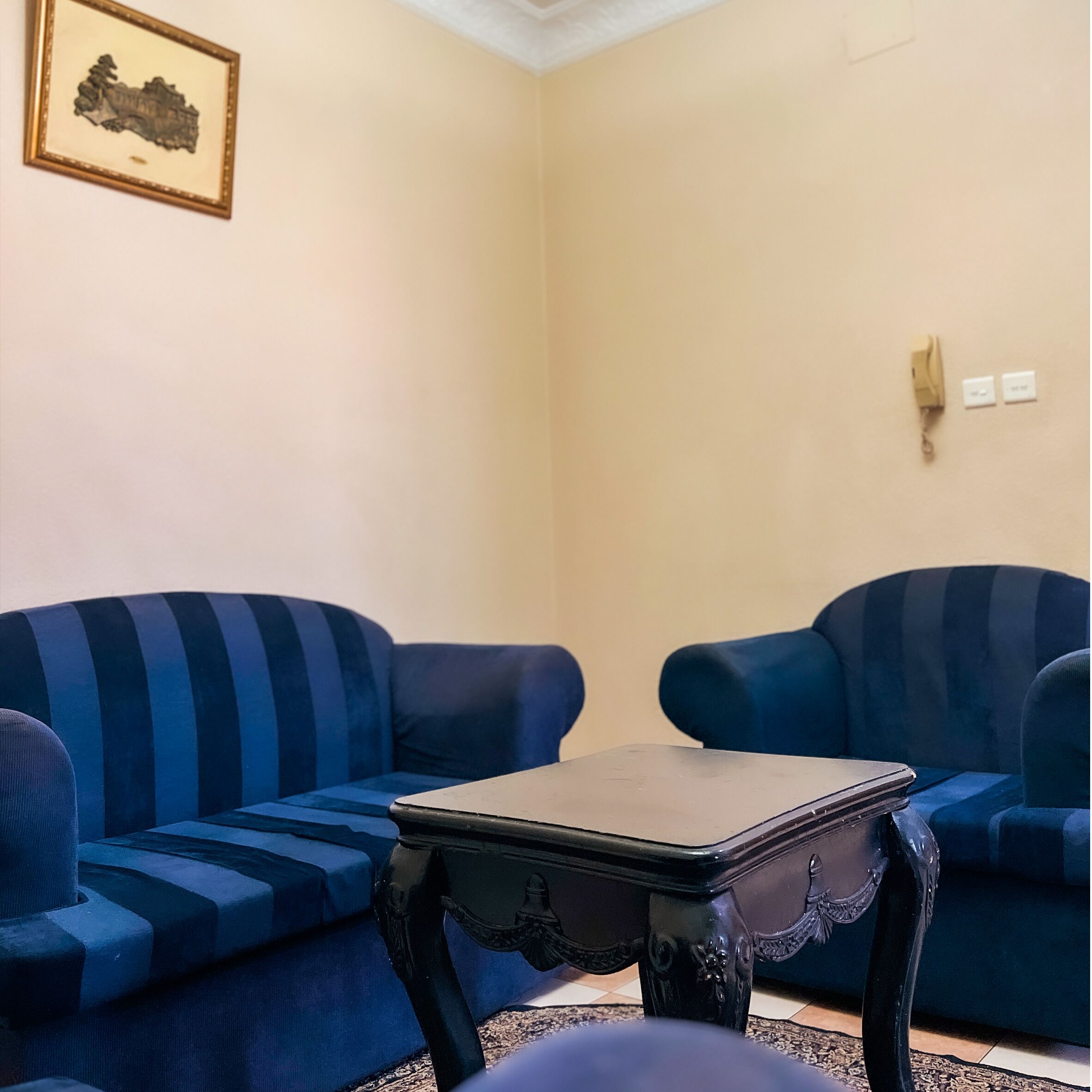 A living room with two blue sofas, a small black table, and a framed picture on the wall.
