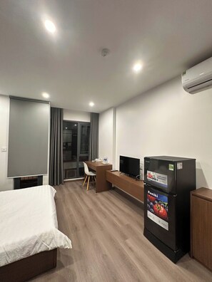 Een hotelkamer met een bed, een bureau met een televisie, een koelkast en een raam met gordijnen.