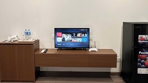A reception desk with a flat-screen TV displaying a streaming service interface, a water dispenser, and a refrigerator. - NQ Apartment (Hanoi)