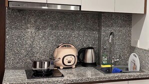 A kitchen with white cabinets, a granite countertop, a kettle, a coffee maker, and a sink. - NQ Apartment (Hanoi)