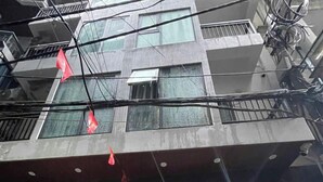 A multi-story building with a closed shutter on the ground floor, a metal staircase, and a red flag on the balcony. - NQ Apartment (Hanoi)