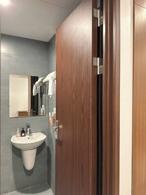 Een badkamer met een houten deur, een wastafel met zeepdispensers en een spiegel.
