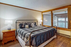 Una camera da letto con una struttura letto in metallo, un comodino in legno con cassetti, un'ampia finestra con persiane e vista sull'esterno.