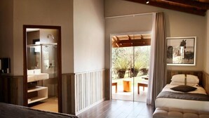 Une chambre d’hôtel avec un lit, une salle de bain dotée d’une douche à parois de verre, un balcon avec une table et des chaises, et un tableau encadré au mur.