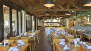 Un restaurant avec des tables et des chaises en bois, un coin bar et une cuisine située au fond de la salle.