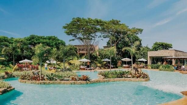 Un complexe hôtelier doté d’une piscine entourée d’une végétation luxuriante et comprenant des espaces de détente.