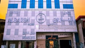 Een hotel met een moderne gevel, met een opvallend logo en borden waarop staat Al Baron Hotel.