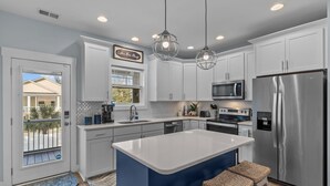 A modern kitchen with white cabinets, a stainless steel refrigerator, a microwave, and a large island with bar stools.