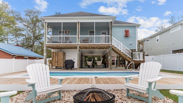 A two-story house with a pool, deck chairs, and a fire pit.