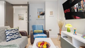 Een moderne woonkamer met een bank, een salontafel met fruit, een televisie waarop Netflix staat en een boekenkast.
