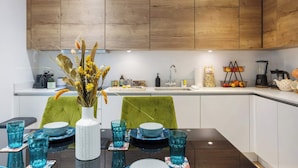 Een moderne keuken met houten kasten, een eettafel gedekt met blauw kristal en een vaas met gedroogde bloemen.