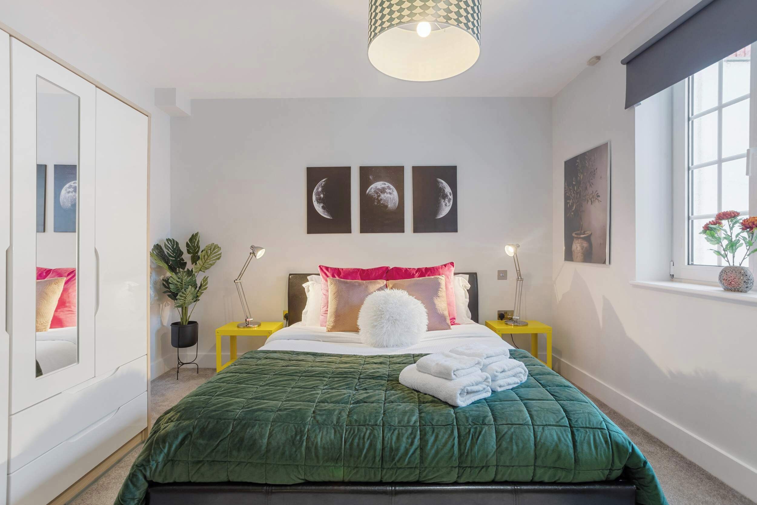A neatly arranged bedroom with a green bedspread, a large mirror, and three wall-mounted moon phase pictures.