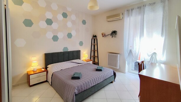 A bedroom with a bed, nightstands, a desk, a radiator, and a window with curtains. - Albi House Vomero modern apartment in the heart of Naples. (Napoli)