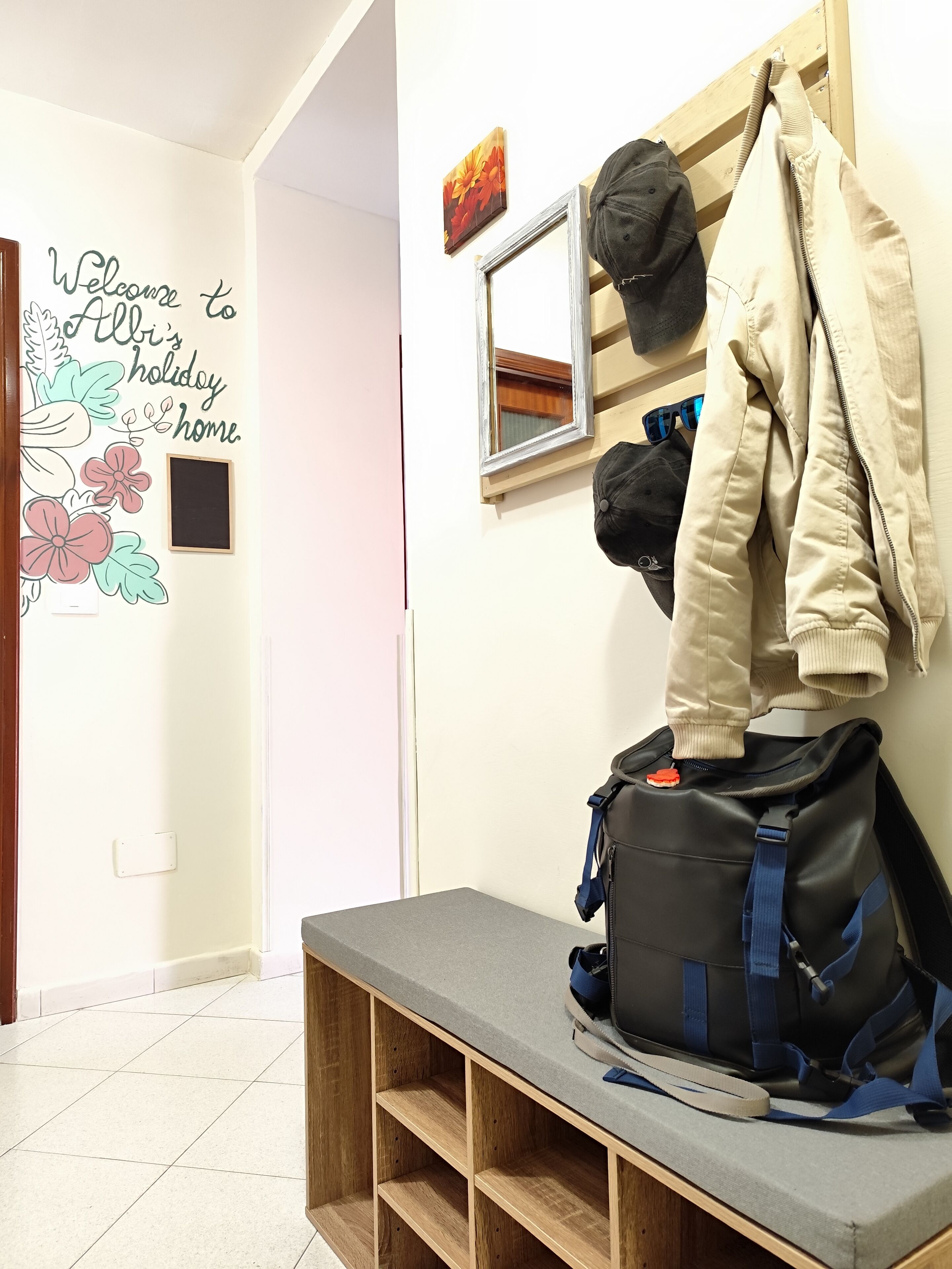 Un couloir avec une pancarte de bienvenue, un miroir et un banc sur lequel sont posés un sac à dos et une veste.