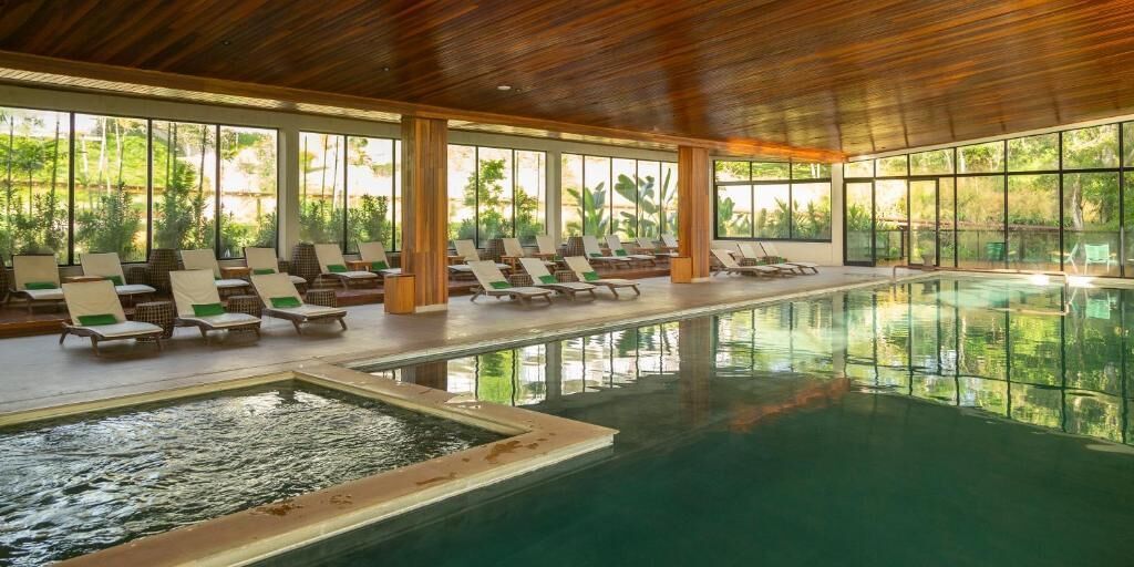 An indoor swimming pool with lounge chairs and large windows.