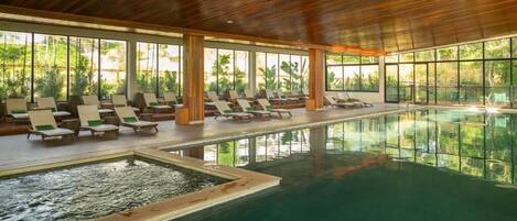 An indoor swimming pool with lounge chairs and large windows.