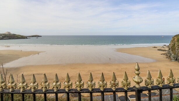 A beach with a clear view of the ocean, a sandy shore, and a distant building on a hill. - Sea Boots (Newquay)