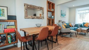 A modern living room with a wooden dining table, matching chairs, a bookshelf, a sofa, and a coffee table. - Sea Boots (Newquay)