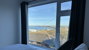 A bedroom with a large window offering a view of a coastal town and the sea. - Sea Boots (Newquay)