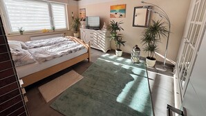 A bedroom with a bed, dresser, TV, and potted plants.