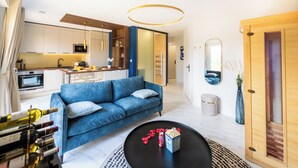 Ein modernes Wohnzimmer mit einem blauen Sofa, einem Couchtisch mit Snacks und einer Küche im Hintergrund.