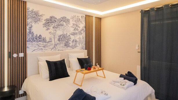 Ein modernes Hotelzimmer mit einem großen Bett, einem Holznachttisch, einem blauen Sessel und einer Decke mit Sternenmuster.