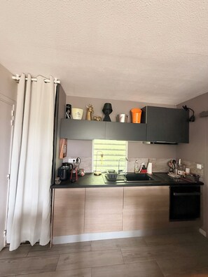 Een moderne keuken met een vast eiland, een zwart aanrecht en een raam met zonwering.