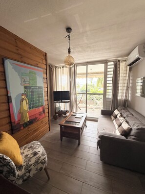 A living room with a sofa, a coffee table, a TV, and a painting on the wall. - Studio overlooking the Marina du Marin (LE MARIN)
