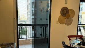 Una cocina moderna con estufa a gas, un comedor con mesa y sillas, y un ventanal corredizo que da a un balcón con vistas a edificios.