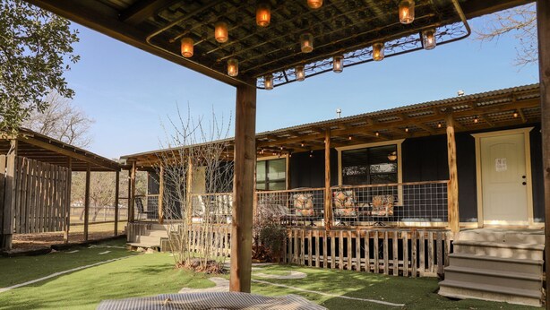 A covered patio area with a grill table, wooden deck, and a view of the building's interior. - Oct Festival HQ 2 blocks from Main St + Fire Pit! (Fredericksburg)