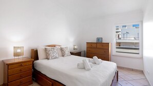 Un dormitorio con cama, mesitas de noche de madera, cómoda y ventana con vistas, además de una lámpara en el techo.