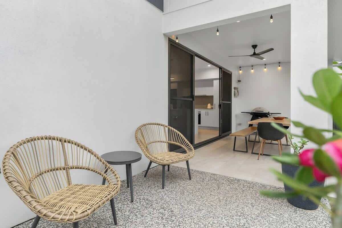 Een modern terras met rieten stoelen en een kleine tafel, een eethoek met een tafel en stoelen, en een plafondventilator.