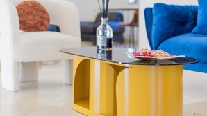 A modern living room with a yellow coffee table, white and blue sofas, and a wooden ceiling beam. - Villa Vetrano – Spacious Apartment in Nola (Cimitile)