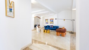 A spacious living area with a blue sofa, a brown ottoman, and a floor lamp. - Villa Vetrano – Spacious Apartment in Nola (Cimitile)