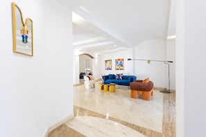 Un amplio salón con un sofá azul, un reposapiés marrón y una lámpara de pie.