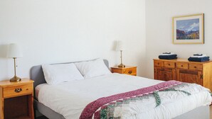 A bedroom with a bed, two bedside tables, a nightstand, a dresser, and a framed picture on the wall.