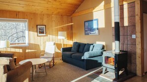 A cozy room with wooden walls and ceiling, a blue sofa, a small table, a chair, a fireplace, and framed pictures on the wall.