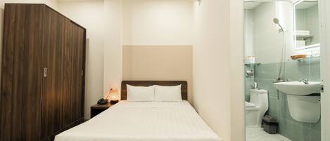 A hotel room with a bed, wardrobe, bedside table, and a bathroom with a sink, toilet, and mirror.
