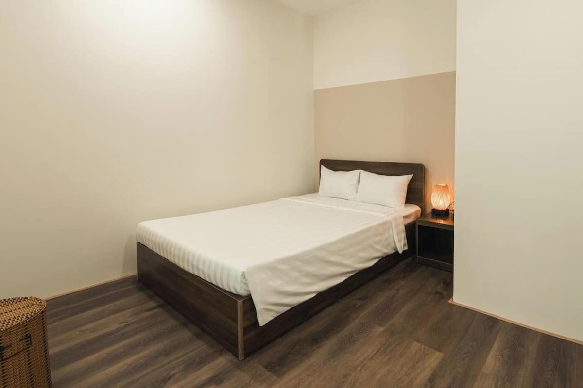 A single bed with a wooden frame, a bedside table with a lamp, and a wicker basket.