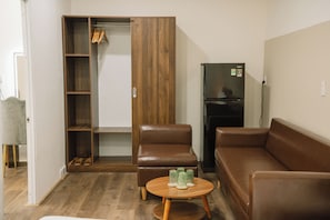 A living room with a brown leather sofa, a wooden coffee table with glasses, a closet with wooden shelves, and a black refrigerator. - Cashew Inn (Ben Thanh)